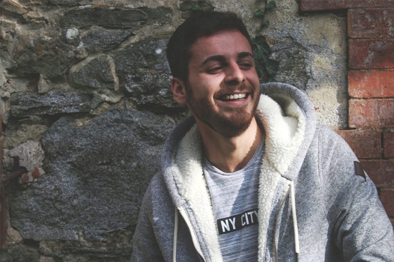 giovane che sorride appoggiato al muro